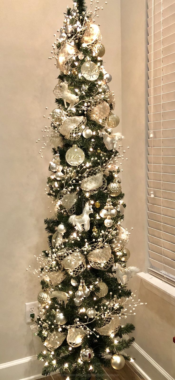 a white christmas tree with silver ornaments on it in a room next to a window