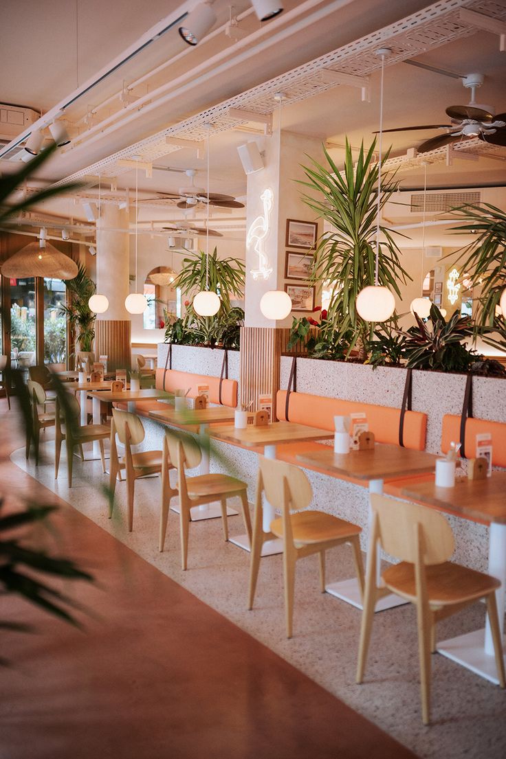 an empty restaurant with wooden tables and plants in the back drop off area on the wall