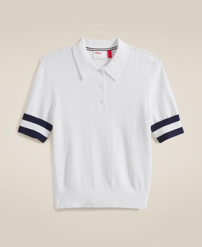 a white polo shirt with navy stripes on the sleeves and collar, in front of an off - white background