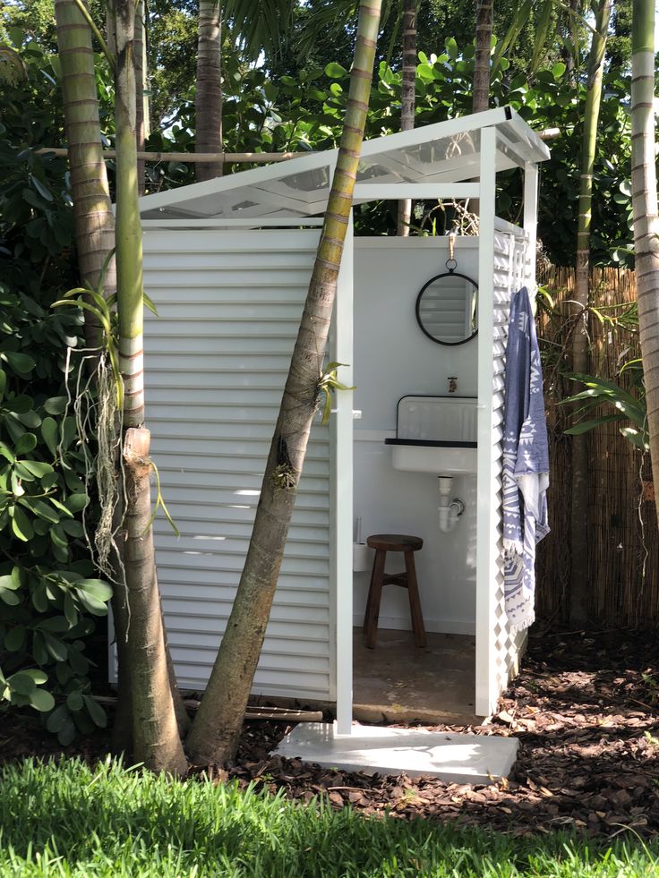 a small white shed with a sink and toilet in the corner between two palm trees