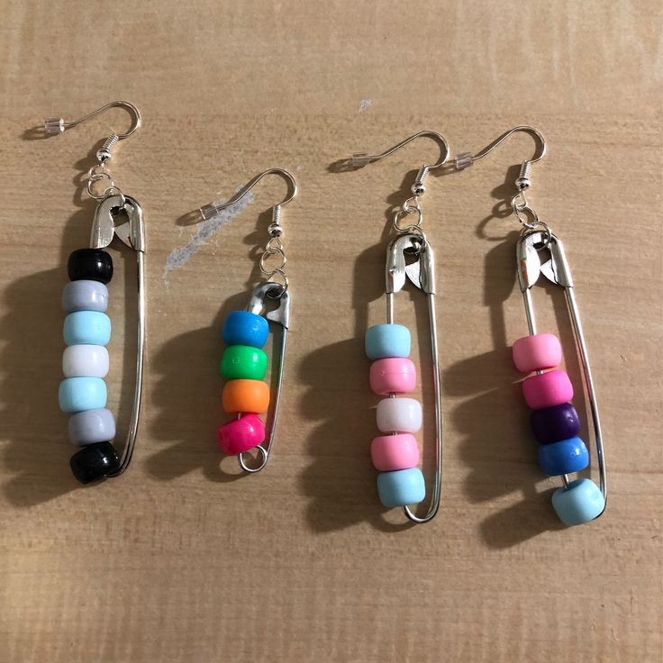 four different colored beads hang from silver earwires on a wooden surface with metal hooks