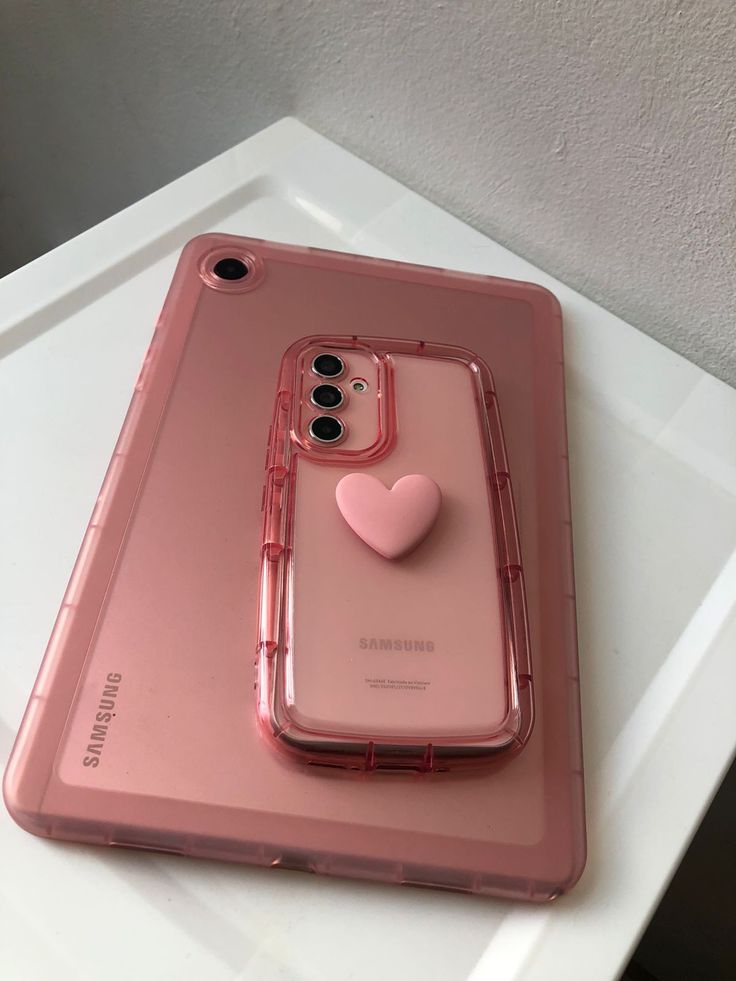 a pink phone case with a heart on the front and back cover sitting on top of it