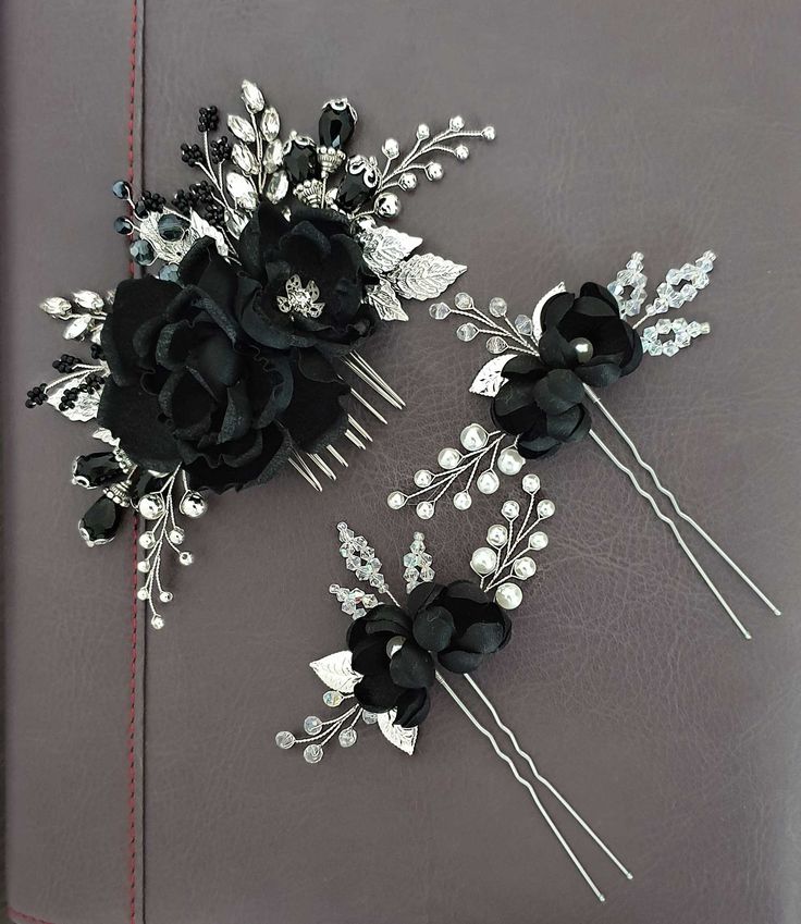 two black flower hair combs on top of a gray leather book with pearls and leaves