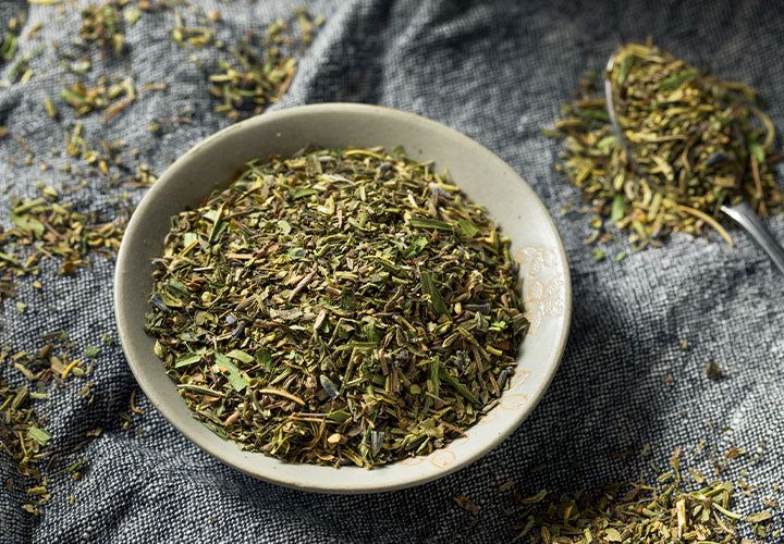 a bowl filled with dried herbs on top of a table next to a spoon and cloth