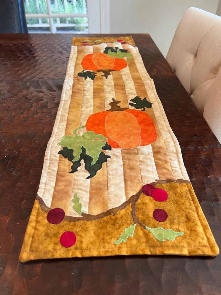 a table runner with pumpkins and leaves on it, sitting on a wooden table