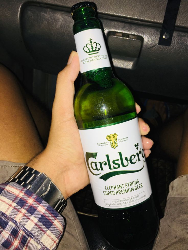 a person holding up a bottle of beer in their hand while sitting inside a car