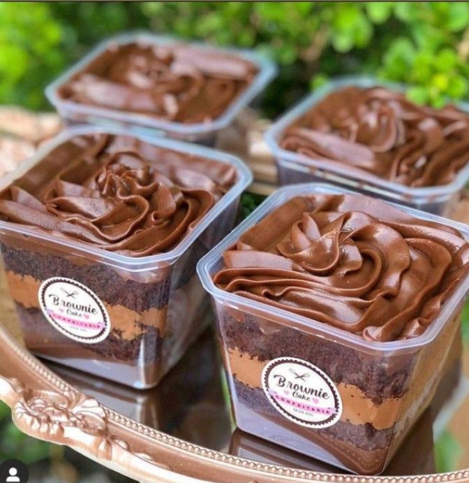 four cupcakes with chocolate frosting in plastic containers on a metal platter