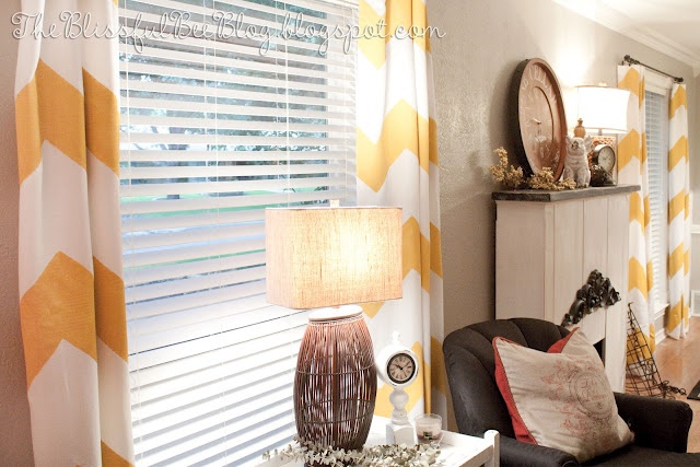 a living room with yellow and white curtains on the window sill, black chair, table lamp and mirror