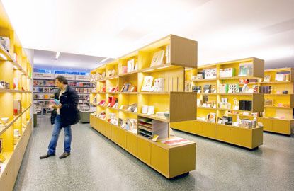 a woman standing in front of a yellow shelf filled with lots of books on it