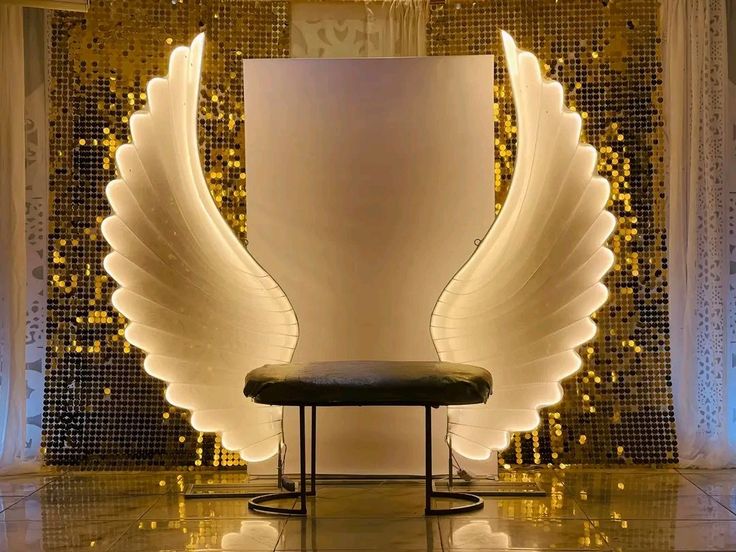 an angel wing sculpture sitting in front of a white wall with gold sequins