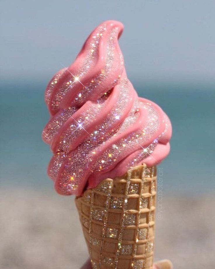 an ice cream cone with pink icing and glitters on it's top