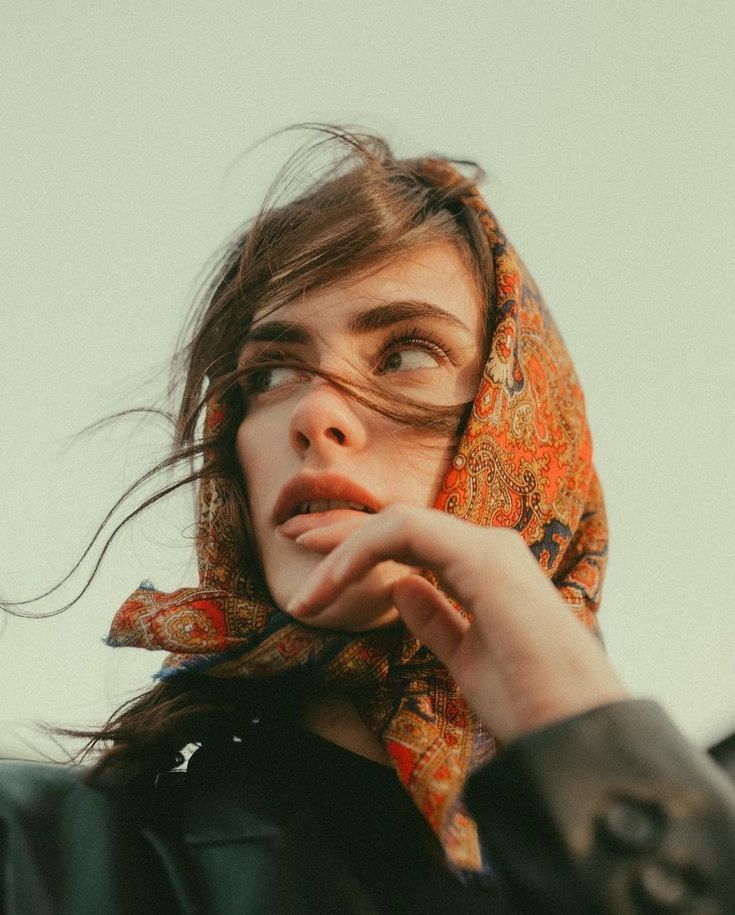 a woman wearing a headscarf looking up at the sky with her hand on her chin