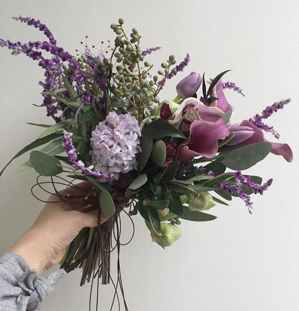 a person holding a bouquet of flowers in their hand with purple and white blooms on it