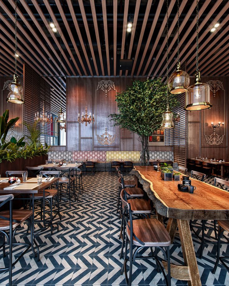 an empty restaurant with wooden tables and chairs, plants on the counter top, and potted trees in hanging lights