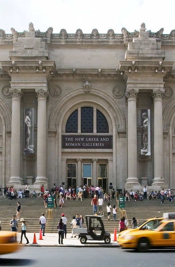 taxi cabs and pedestrians in front of an old building with columns on the facade