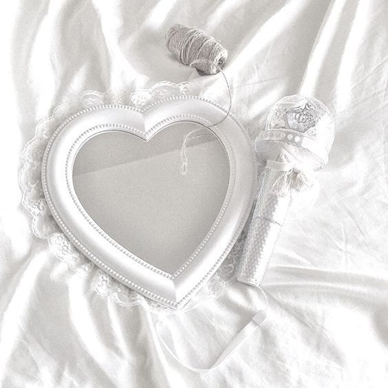 a white heart shaped mirror sitting on top of a bed next to a spool of thread