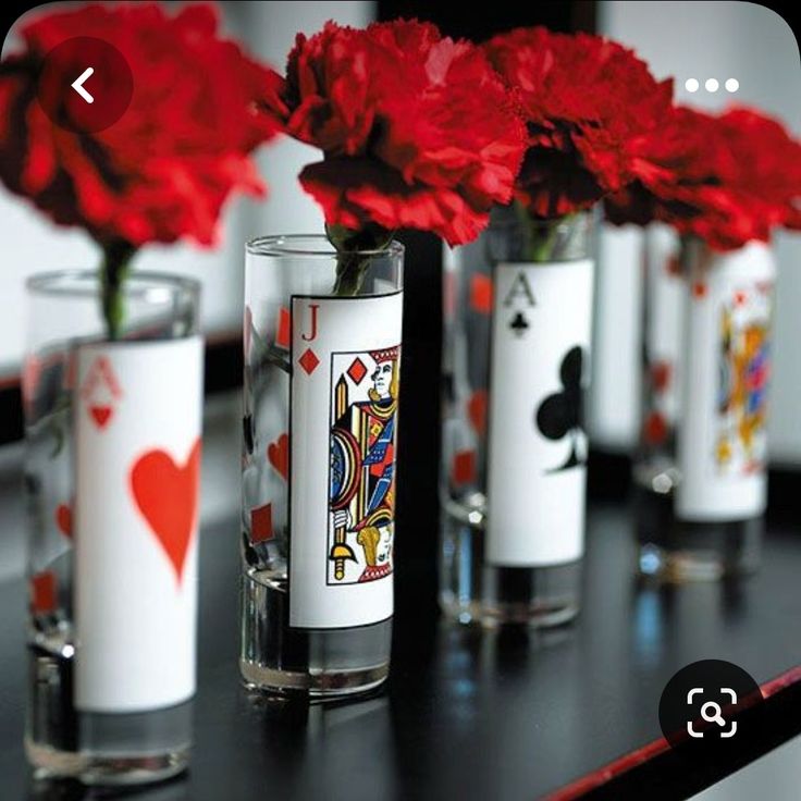 four vases with playing cards and red flowers in them are on a black table