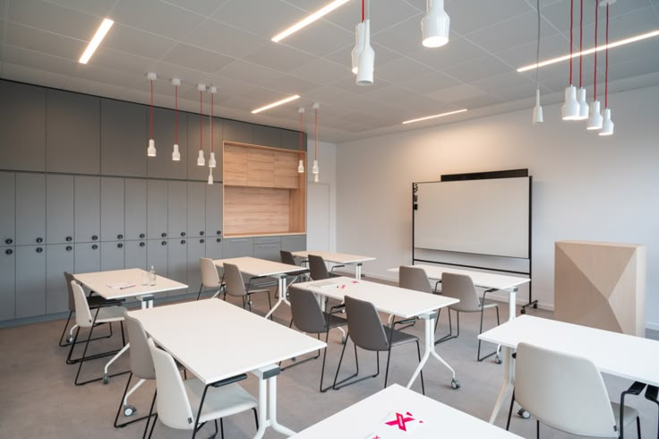 an empty classroom with desks and chairs in front of a whiteboard on the wall