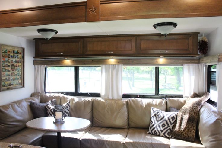 a living room with couches, tables and windows in the back wall is lit by recessed lights