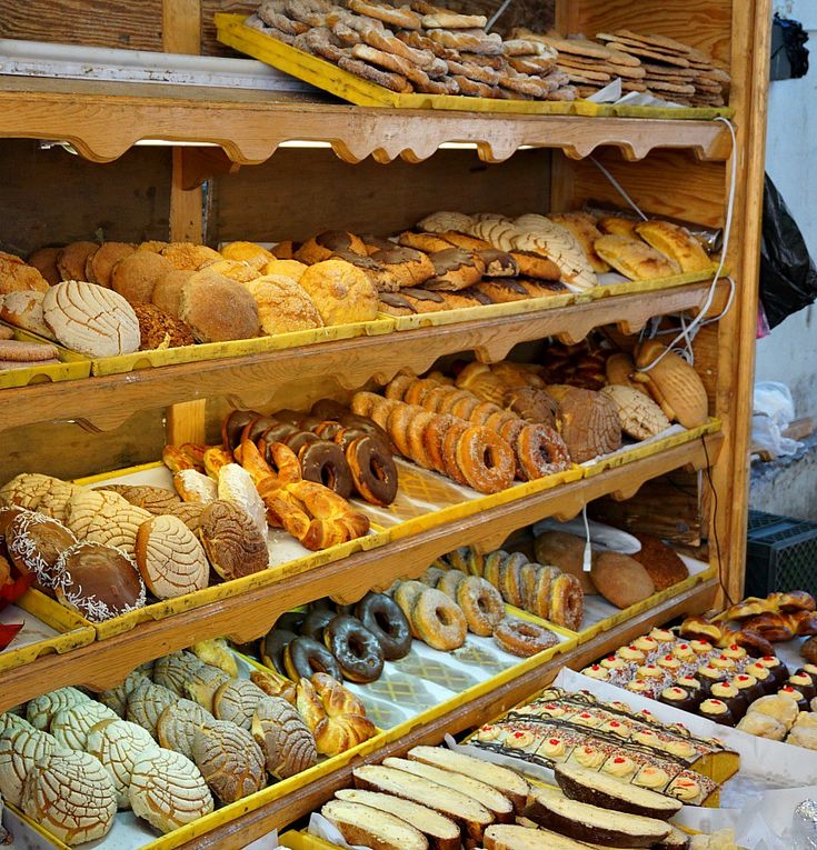 many different types of pastries are on display in a bakery case with wooden shelves