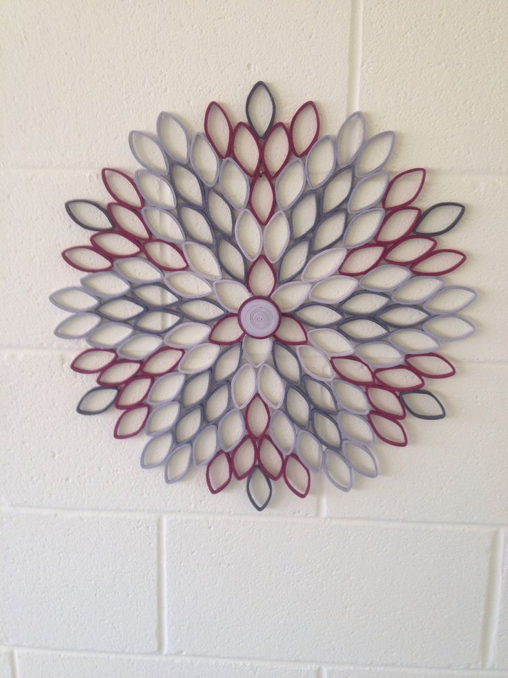 a metal wall hanging with red and grey petals on it's side against a white brick wall