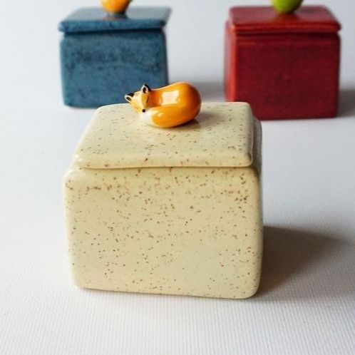 three small ceramic containers sitting on top of a white table next to apples and oranges