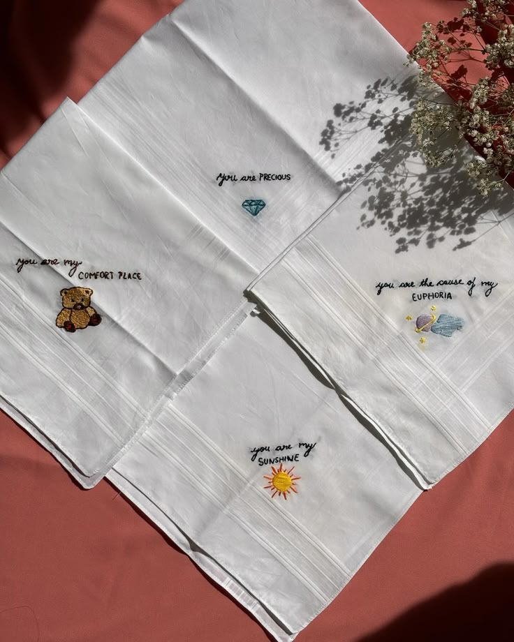 four white napkins with embroidered designs on them and a small tree in the middle