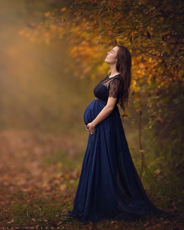 a pregnant woman in a blue dress is looking up into the sky while standing on a path