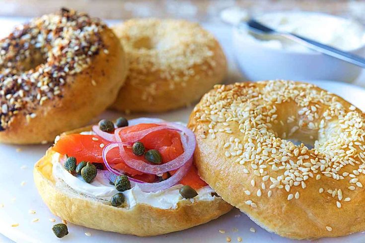 three bagels with different toppings are on a white plate next to a fork