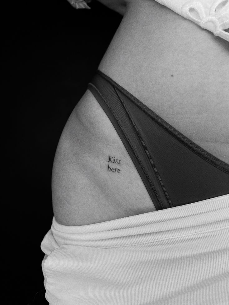 a woman's stomach with the words kiss here tattooed on her lower side belly