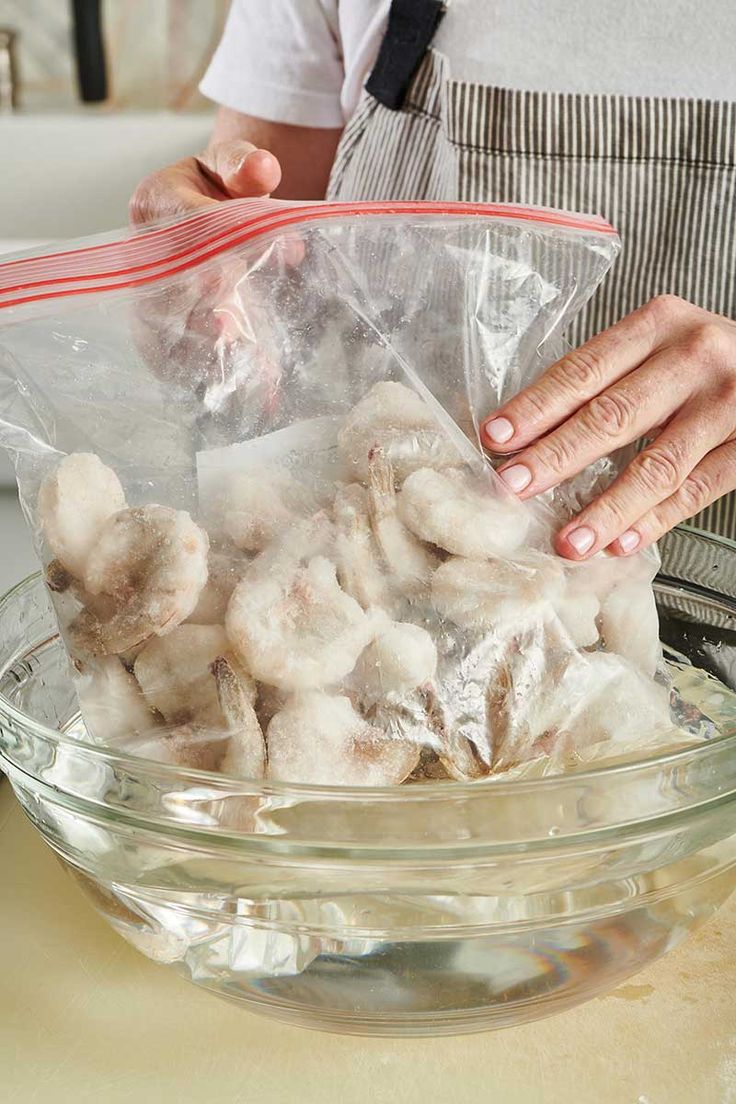 a person holding a plastic bag filled with cotton balls in a bowl on top of a counter