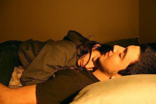 a man and woman laying on top of a bed next to each other with their eyes closed