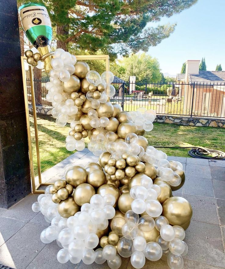 a large pile of gold and white balloons sitting on top of a sidewalk next to a mirror