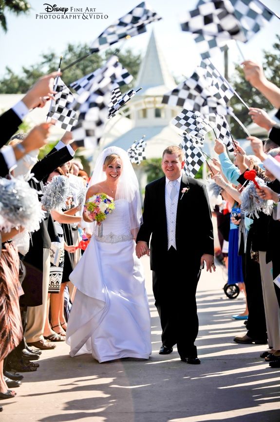 a bride and groom walking down the street with their wedding party waving checkered flags