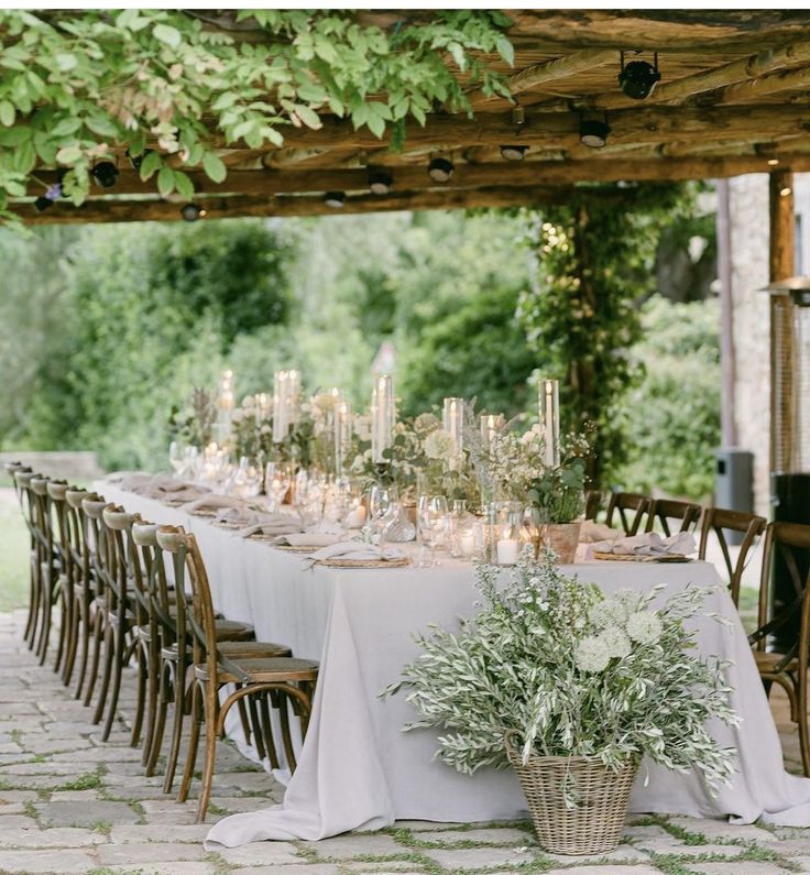 a long table with white linens and greenery is set up for an outdoor dinner