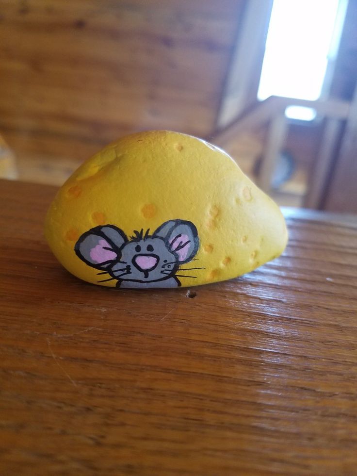 a rock with a cartoon mouse painted on it sitting on a wooden table next to a window