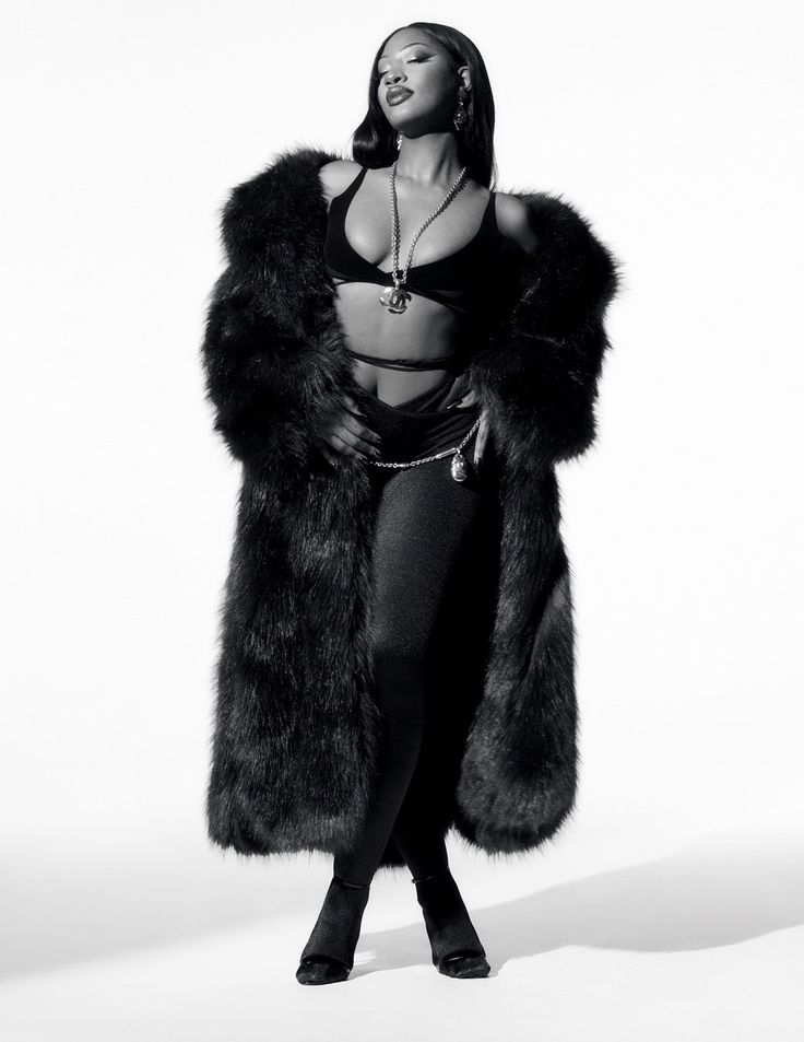 a black and white photo of a woman wearing a fur coat with her hands on her hips