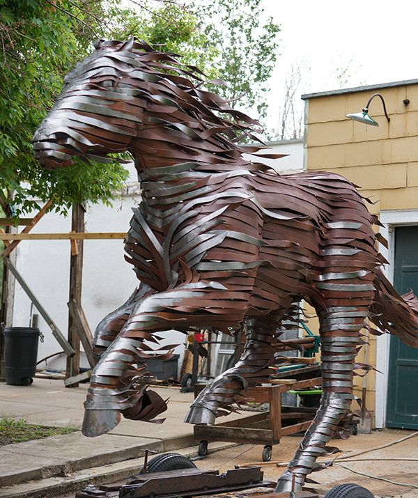 a large metal horse statue sitting on top of a pile of wood planks in front of a building