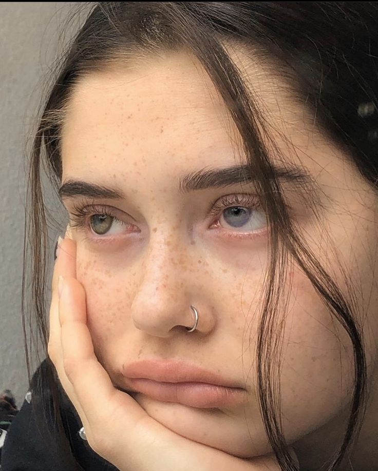 a woman with freckles and piercings on her nose looking at the camera