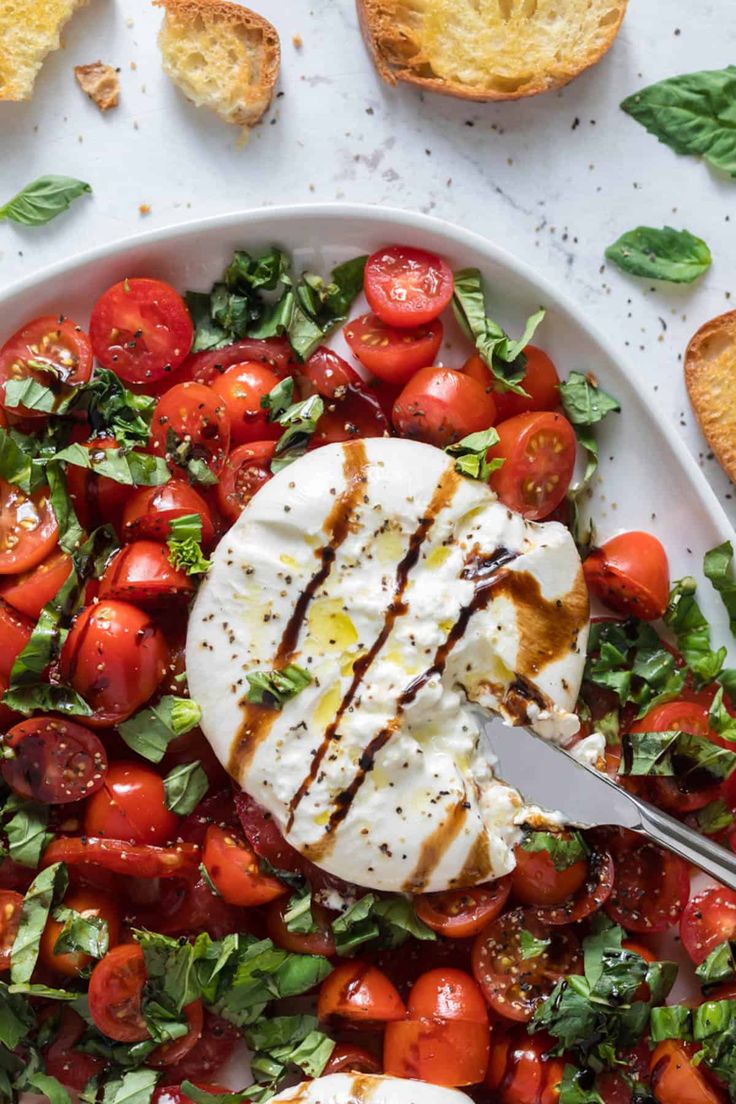 a white plate filled with tomatoes and bread on top of a marble table next to a fork