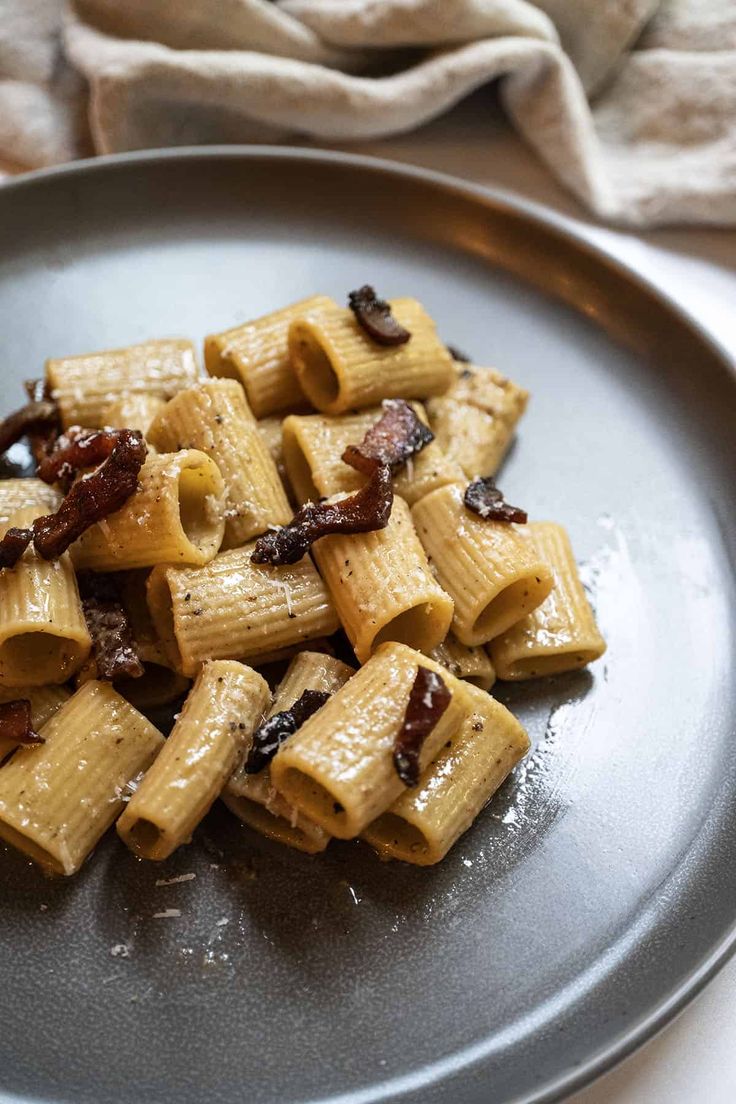 a plate full of pasta with bacon and sauce on the side, ready to be eaten