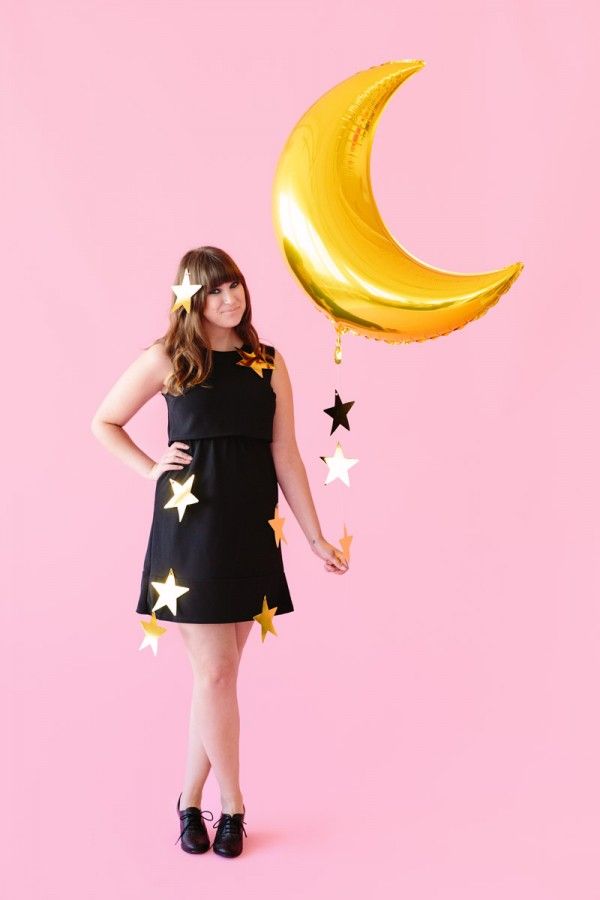 a woman in a black dress is holding a yellow balloon with stars on it and the moon above her