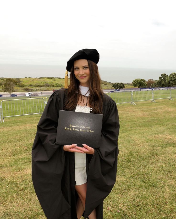 a woman wearing a graduation gown and holding a plaque in front of the camera on grass