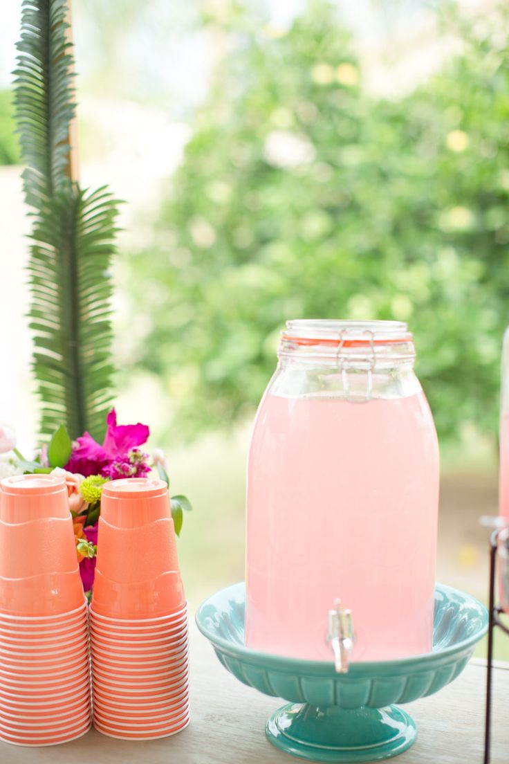 there is a pink drink in a glass jar on the table next to orange cups