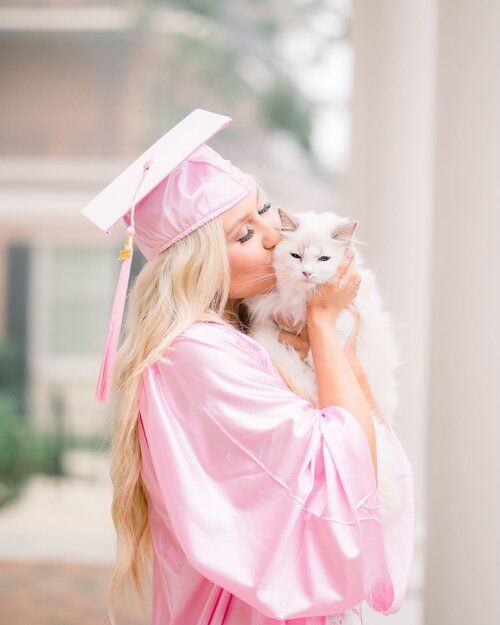 a woman in pink graduation gown holding a white cat