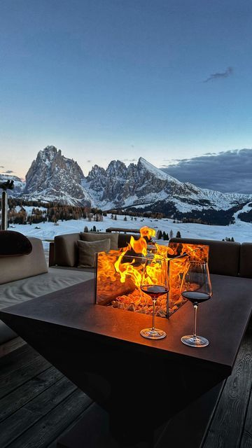 two glasses of wine sit on an outdoor table with mountains in the background at night