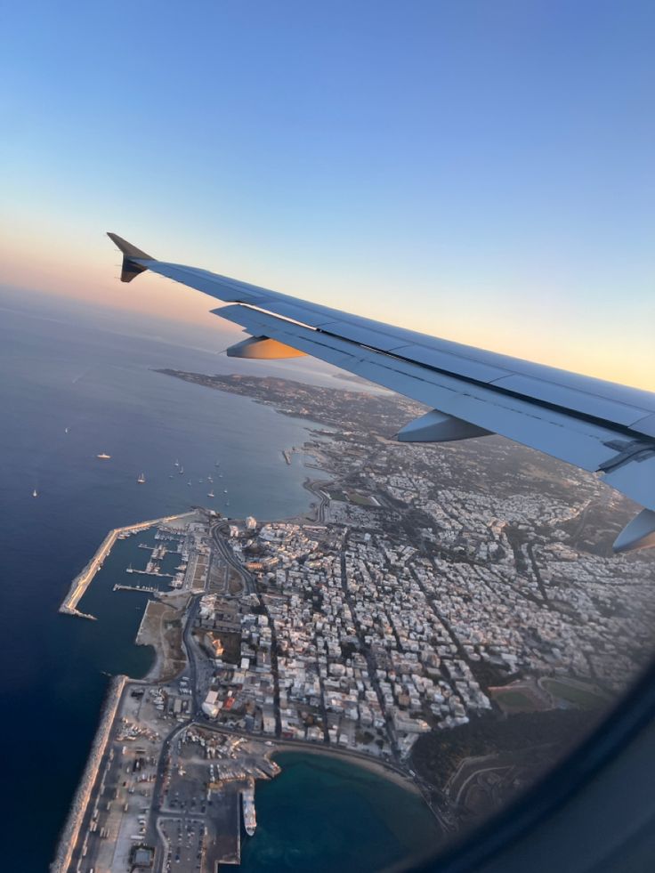 the wing of an airplane flying over a city next to the ocean and land area