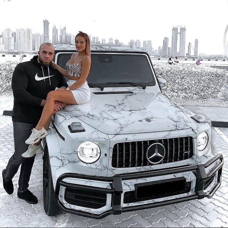 a man and woman sitting on the hood of a white mercedes g63 amg