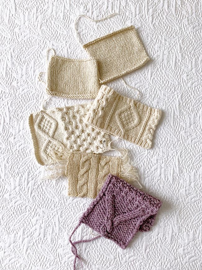 four knitted items laid out on a white tablecloth, including gloves and mittens