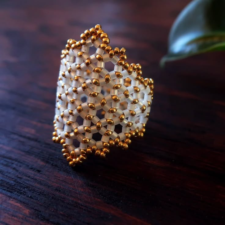 a white beaded ring sitting on top of a wooden table next to a plant